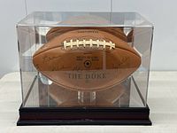 Front view of signed football inside clear acrylic display case on wood base