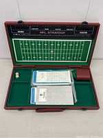 Open view of the NFL Strategy Game showing the football field playboard printed inside the case lid. Multiple decks of game cards, a single six-sided die, and dice cup are arranged in the compartment below the field