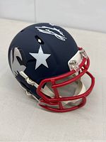 Angled front right view showing navy blue shell, silver logo decal, silver autograph on top, red facemask