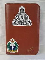 Brown zip-up case featuring military insignias and initials on front