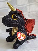 Front and side view of black scaled textured Ty Beanie Boo dragon plush with gold horn and red glitter wings, showing Ty heart-shaped tag.