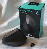 Front and side view of Logitech MX Vertical ergonomic mouse next to its box and USB wireless receiver on white surface.