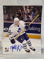 Photo showing Matt Stajan skating on ice in white Toronto Maple Leafs uniform with autograph in blue ink at bottom center.