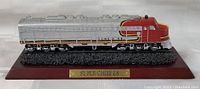 Front and side view of the Super Chief E8 Santa Fe model train on wood display stand showing painted details, base texture, and plaque