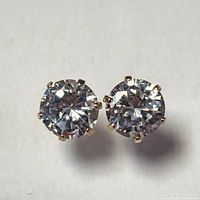 Pair of round cubic zirconia stone stud earrings set in 10K yellow gold prong settings photographed on a white background.