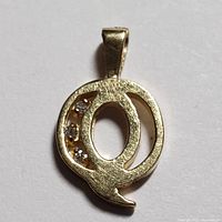 Close-up image of a 10K yellow gold pendant shaped as the letter Q with three small diamonds embedded on the left curve.