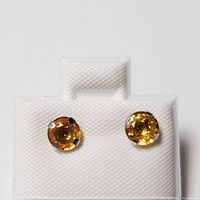 Front view of pair of yellow gold stud earrings featuring round fancy color sapphires mounted in prong settings on white display card.