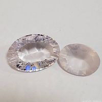 Two amethyst gemstones placed on white background, showing clarity and shape difference. One oval faceted, the other round faceted.