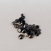 Collection of small round faceted black diamond gemstones shown on a white background