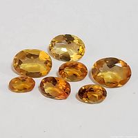 Seven loose oval faceted citrine gemstones arranged on white background showing variety of sizes and rich golden to amber color hues.