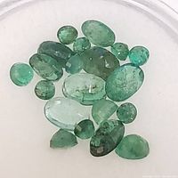 Close-up photo of various loose emerald gemstones showing different cuts and inclusions.