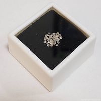 White container holding multiple small loose diamonds on black background.