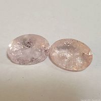 Two faceted oval morganite gemstones lying side by side on a white background, showing color and internal inclusions.