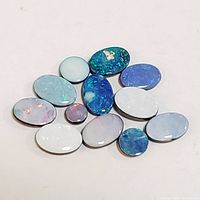 Top view of 13 loose oval opal gemstones of various sizes and colors on a white background