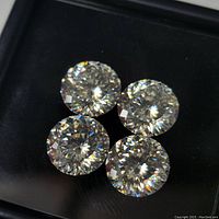 Four laser cut round moissanite stones placed on a dark surface, showing facets and gem sparkle.