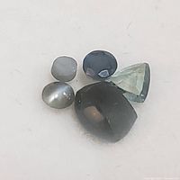 Close-up photo showing 5 cat's eye alexandrite gemstones on a white background with clear details of cut and color.