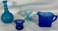 Image showing four antique glass items: hobnail turquoise bottle, cobalt blue jug, curved blue ashtray, and small hobnail turquoise vase