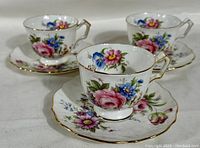 Front angle of 3 Aynsley tea cup and saucer sets with colorful floral bouquets and gold trim on bone china.