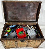 Open wooden chest filled with assorted Lego pieces including bricks, plates, and parts in various colors.