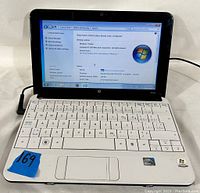 Front view of HP Mini laptop open, showing keyboard, trackpad, and screen displaying Windows 7 Starter system info.