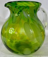 Front view of large green blown glass pitcher with applied clear handle, showing mottled color patterns and rounded shape.