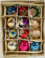 Top view of the box showing the 12 vintage glass Christmas ornaments in individual compartments with varied colors and glitter decorations.