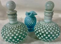 Front view of the two hobnail glass bottles with stoppers and small hobnail vase between them.