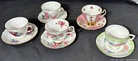 Five fine bone china tea cups and matching saucers with floral designs arranged in a single photo on black background.