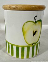 Front view of the ceramic jar showing the green and yellow apple design with a wooden lid.