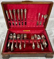 Full view of wooden chest open showing all flatware pieces inside arranged in slots on red velvet lining