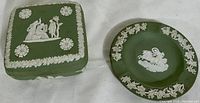 Top-down view showing the covered trinket box with classical white relief figures and floral motifs and the round ash tray with matching decoration