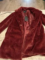 Top view of the plush burgundy winter coat showing lapel collar, inside satin lining and brand tag.