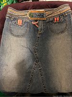 Full view of the folded denim skirt showing the faded blue wash, front pockets, and decorative waistband and belt loops.