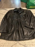 Black leather coat spread out on floor, showing overall shape and condition