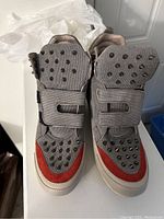 Top view of pair of grey fabric Hush Puppies sneakers with velcro straps, black studs on tongues, red toe accents, and white soles