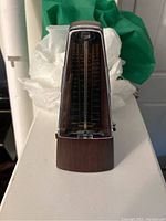 Front view of mechanical metronome showing tempo scale and pendulum arm inside plastic cover with wood grain body.