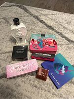 Lot of new cosmetics arranged on carpet, including Anna Sui lotion, eyeshadow palettes from NYX, Trend Beauty, Steve Laurant, and a Fenty Beauty box