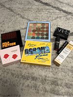 Overview photo of all cosmetic items showing various palettes and boxed lip products on carpet floor.