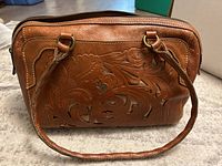 Front view of brown leather purse showing intricate floral tooled and cutout pattern with gold background and double straps.