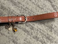 Close-up of pink leather belt with embossed double-G logos and chain with bee charm near the buckle.