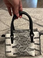 Black and white snake print Guess handbag with two black handles held up by a hand, showing overall style and shape.