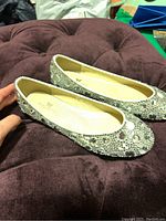 Pair of sparkly flats on dark purple padded surface, showing top view with heavy rhinestone embellishments.