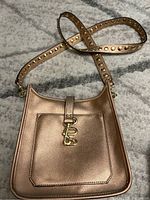 Rose gold shimmery Steve Madden crossbody bag laid flat showing front with decorative buckle and pocket.
