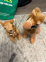 Both stuffed animals, the kangaroo sitting with a visible joey in pouch, and the camel standing with fluffy mane, showing front and side views.