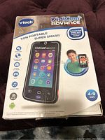 Box front view depicting Vtech KidiCom Advance children's smart portable device with icons, uses, age range 4-9 years.