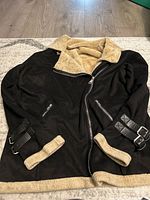 Full view of black winter jacket showing asymmetrical zipper, beige flocked interior on collar, cuffs, and hem, and zipped pockets.