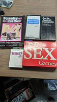 Five adult-themed games on a wooden surface: Foreplay, New Phone Who Dis?, Cards Against Humanity, Meme?, and 1000 Sex Games.