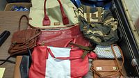 Multiple bags and pocketbooks displayed on table showing variety in size, design, and material