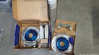 Big Brake Kit components including drilled and slotted brake discs with blue anodized centers and caliper bracket hardware inside original boxes.