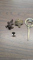 Four brass items including Coca Cola wall mount bottle opener, dragon figurine, decorative finial, and horseshoe key holder placed on wood surface.